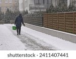 Photo of a man from behind pouring sand on a slippery sidewalk, preventing fractures and injuries during black ice and snowfall.