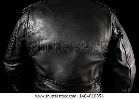 Photo of a man in black leather biker jacket standing on neon lightened night street background rear view.