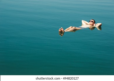 Photo Of The Man Floating And Relax In Water Dead Sea. Tourism Recreation, Healthy Lifestyle Concept. Copy Space. Focus On Feet