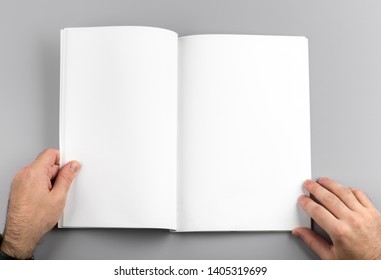 Photo. Man Holds Open Journal. For Graphic Designers Presentations And Portfolios. Mock Up Of Empty Magazine. Blank Book Mockup Isolated On Gray Background.