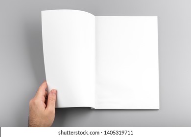 Photo. Man Holds Open Journal. For Graphic Designers Presentations And Portfolios. Mock Up Of Empty Magazine. Blank Book Mockup Isolated On Gray Background.