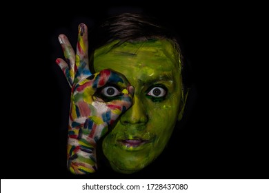 Photo of a man's face in a dark key on a black background. Face and hand are painted with colored paints. Creative photo of a man in minimalistic black. - Powered by Shutterstock