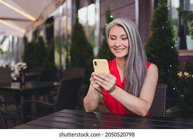 Photo of mature attractive asian woman happy positive smile look read browse smartphone sit cafe rest outdoors