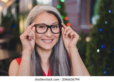 Photo of mature cheerful asian woman happy positive smile hands put eyeglasses vision summer outdoors