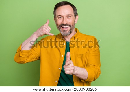 Photo of mature man happy positive smile show call phone sign point finger you isolated over green color background