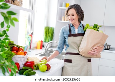 Photo of mature pretty lady hold fruit wear apron jean shirt at kitchen alone