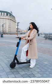 
Photo of a mature woman in a light coat riding a scooter outdoors on a city street