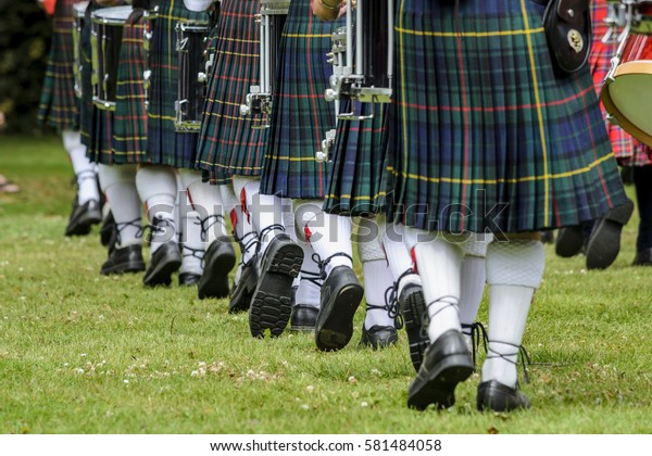 Photo of men below waist in green kilts and\
white socks are marching in New\
Zealand