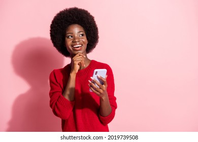 Photo Of Minded Happy Dark Skin Woman Look Empty Space Hold Hand Chin Phone Isolated On Pink Color Background