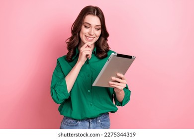 Foto de una inteligente mujer inteligente de mente inteligente con el pelo ondulado vestido de camisa verde mirar el tablet elegir el producto aislado en el fondo rosado