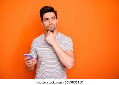 Photo Of Minded Serious Millennial Guy Hold Telephone Deep Think New Instagram Blog Post Text Arm On Chin Look Side Wear Striped T-shirt Isolated Bright Orange Color Background