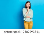 Photo of minded woman with bob hairstyle dressed teal shirt look at logo empty space finger on chin isolated on blue color background