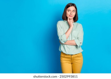 Photo of minded woman with bob hairstyle dressed teal shirt look at logo empty space finger on chin isolated on blue color background - Powered by Shutterstock