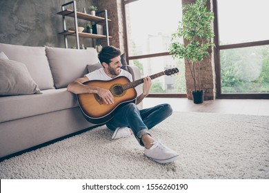 Photo of mixed race guy sitting floor leaning sofa hold acoustic instrumental guitar playing new written song sound signing creative talented person flat loft living room indoors