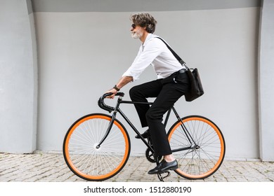 Photo of modern old businessman in sunglasses riding bicycle over gray wall on city street - Powered by Shutterstock