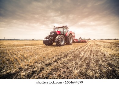 Photo of modern red tractor in the field after harvest seeding directly into the stubble using GPS for precision farming during cloudy summer/autumn day. 