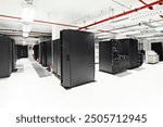 A photo of a modern server room with rows of black server racks and a visible fire suppression system with red pipes running along the ceiling. The room has a clean, professional appearance with white