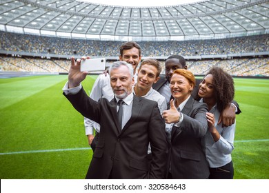 Photo Of Multi Ethnic Business Group. Mixed Race Business Team Making Photo On Mobile Phone. Business People Standing On Modern Sport Track. Accent On Leader Of Group. Stadium As A Background