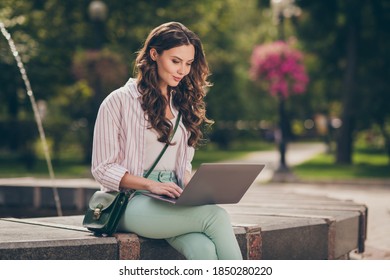 Photo Of Nice Brunette Hair Young Lady Sit Near Fountain Work Study Writing Laptop Wear Green Pants Shirt Top Bag In Park Outdoors