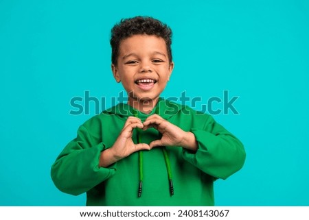Photo of nice cheerful schoolboy with wavy hair dressed green pullover fingers show heart symbol isolated on teal color background