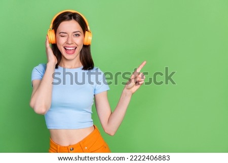 Photo of nice positive girl eye wink indicate finger empty space isolated on green color background