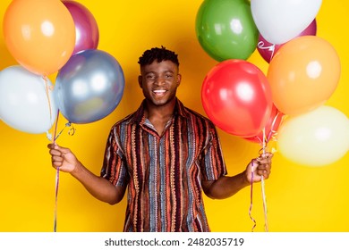 Photo of nice young man hold balloons wear shirt isolated on yellow color background - Powered by Shutterstock