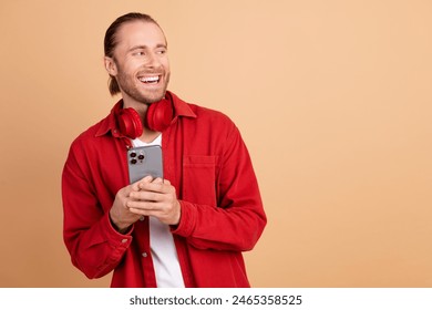 Photo of nice young man phone headphones look empty space wear red shirt isolated on beige color background - Powered by Shutterstock