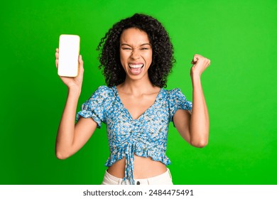 Photo of nice young woman raise fist empty space phone screen wear top isolated on green color background - Powered by Shutterstock