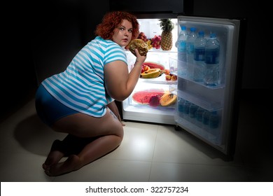 Photo at night of Overweight woman opening refrigerator and looking for a late supper