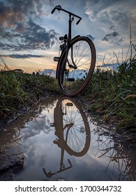 Photo Of An Old Bicycle And Its Reflection In A Puddle Of Water,with Background Of Dusk Sky.