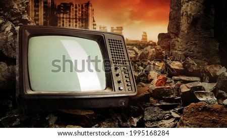 Photo of old fashioned tv set laying on pile of bricks on ruined city wasteland background.