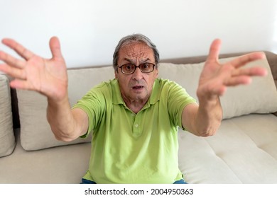 Photo of a old man arguing, shouting, angry and emotionally gesturing at home. Irritated senior man in casual clothes at home wear glasses, yelling while sitting at home isolated on bright background.