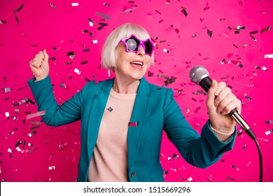 Photo Of Old Mature Stylish Energetic Woman Singing In Microphone Wearing Star Shaped Spectacles Standing In Falling Confetti Isolated Over Pink Vivid Color Background