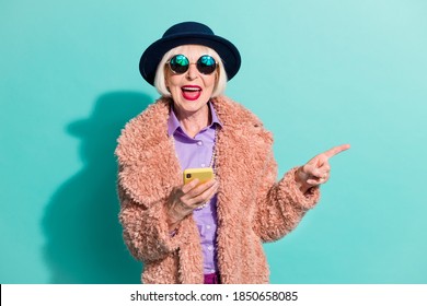 Foto de anciana vistiendo ropa interior vintage sosteniendo un gadget apuntando al espacio vacío aislado color turquesa fondo