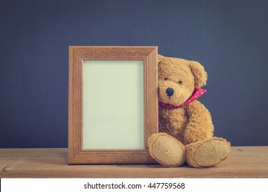 Photo Old Wood Frame With Single Brown Teddy Bear Sitting On Old Wooden Table, Black Background. Emphasizing Copy Space For Write Text. Image Style Vintage.