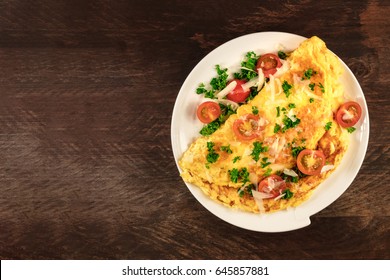 A photo of an omelette with cherry tomatoes, parsley. and grated cheese, shot from above on a rustic wooden texture with a place for text - Shutterstock ID 645857881