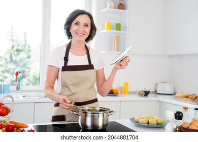 Photo of optimistic agee brunette lady cook potatoes wear apron white t-shirt at kitchen alone - Powered by Shutterstock