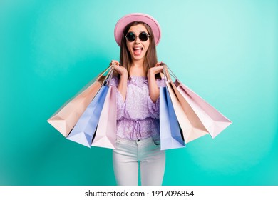 Photo of optimistic brunette girl hold bags open mouth wear purple shirt cap trousers spectacles isolated on blue color background