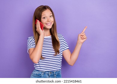 Photo Of Optimistic Girl With Straight Hairdo Wear Striped T-shirt Talk On Phone Directing Empty Space Isolated On Purple Color Background