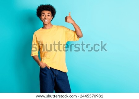 Photo of optimistic guy with afro hairdo dressed yellow t-shirt showing thumb up hand in pocket isolated on turquoise color background