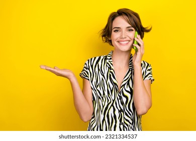 Photo of optimistic pleasant lovely girl palm demonstrate offer empty space talking on smartphone isolated on yellow color background - Shutterstock ID 2321334537