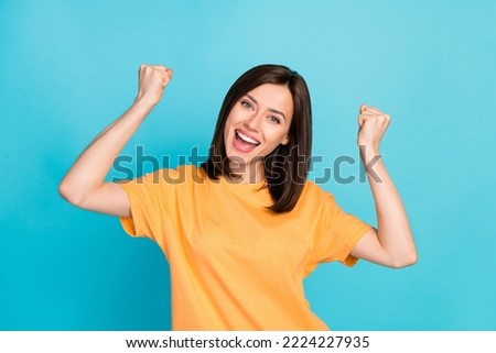 Photo of optimistic satisfied pretty girl with straight hairdo dressed yellow t-shirt raise fists isolated on blue color background