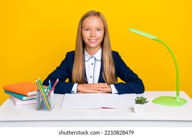 Photo Of Optimistic Smart Clever Schoolgirl With Straight Hairdo Wear Blue Blazer Sitting At Desk Isolated On Yellow Color Background