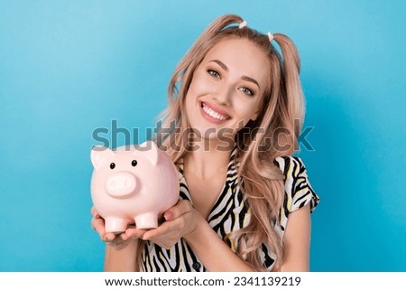 Photo of optimistic toothy beaming girl dressed striped blouse hands hold piggy bank saving money isolated on blue color background
