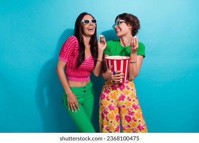 Photo of optimistic two young girlfriends laughing enjoy watching 3d cartoons eating biting popcorn isolated on blue color background - Powered by Shutterstock