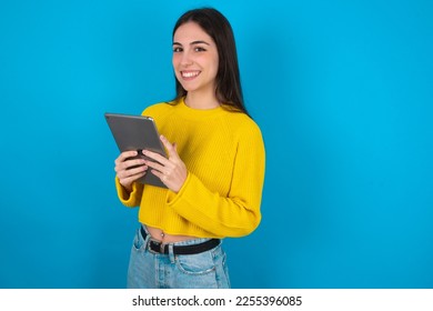 Photo of optimistic Young caucasian woman wearing yellow sweater over blue background hold tablet - Powered by Shutterstock