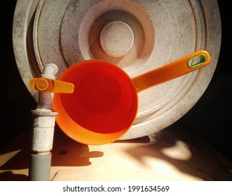 Photo Of An Orange Dipper, A Water Faucet With An Orange Handle, And A Dull White Bucket Lid At The Daylight. Equipment In The Kitchen. View From Above. Focus On Foreground.