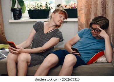 Photo Of Ordinary Family Relationships. Mom And Teen Look At The Phone Of Their Son At Home While Sitting On The Sofa