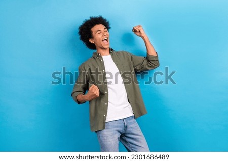 Photo of overjoyed funky guy with curly hairstyle dressed stylish shirt raising fists eyes win betting isolated on blue color background