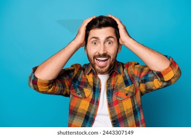 Photo of overjoyed man with beard dressed plaid shirt hold hands on head staring at awesome sale isolated on blue color background - Powered by Shutterstock